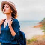 Mid adult woman in coastal setting, carrying backpack, breathing in fresh air