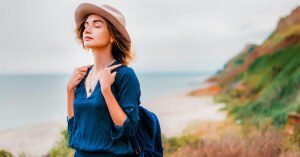 Mid adult woman in coastal setting, carrying backpack, breathing in fresh air